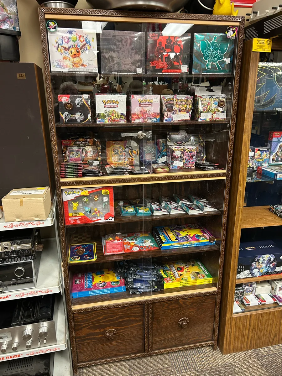 Tall display cabinet filled with sealed Pokemon products at Krave Antiques Regina